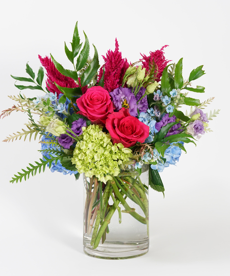 unique floral arrangement of blue hydrangea, purple lisianthus, and hot pink roses arranged in a clear glass vase