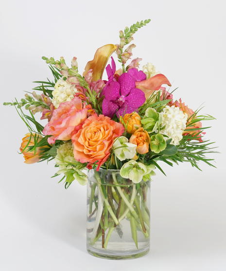 pink orchids, orange roses, and mango calla lilies arranged in a clear glass vase