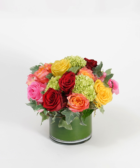 low and lush arrangement of red, orange, yellow and pink roses accented with ivy and mini green hydrangea