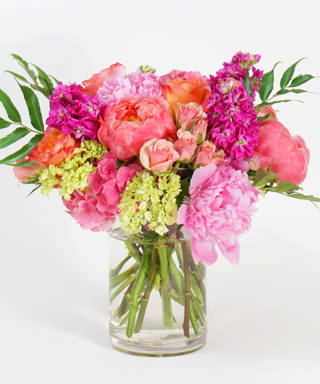 colorful spring floral arrangement featuring orange roses, hot pink peonies, and gloriosa lilies with seasonal greens