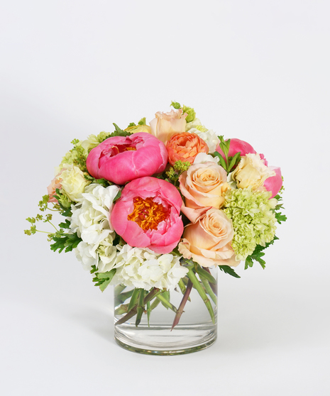 coral peonies, peach roses and white hydrangea arranged in a clear glass vase