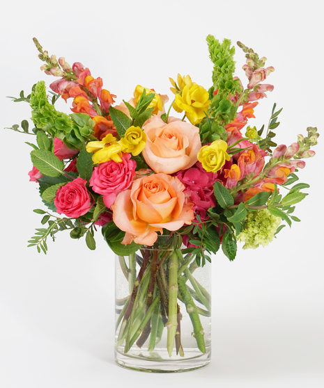 floral design of coral roses, peach ranunculus, and hot pink hydrangea and arranged in a clear glass vase