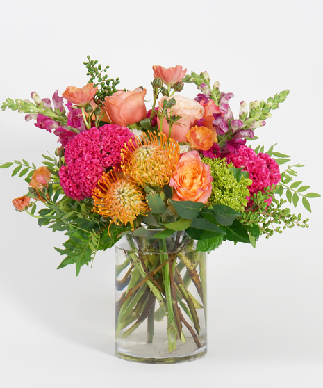 colorful fall floral design of orange roses, protea, hot pink coxcomb, and burgundy snapdragon with textural greens