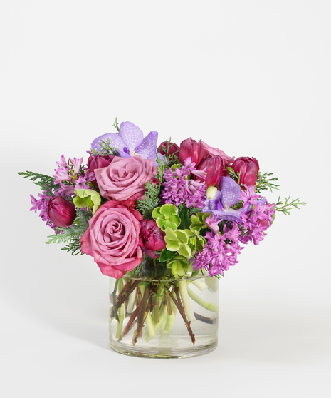 purple hyacinth, lavender roses, and plum orchids arranged in a black stone container and accented with winter greens