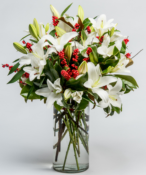 white lilies, magnolia, and red winterberry in a tall glass vase
