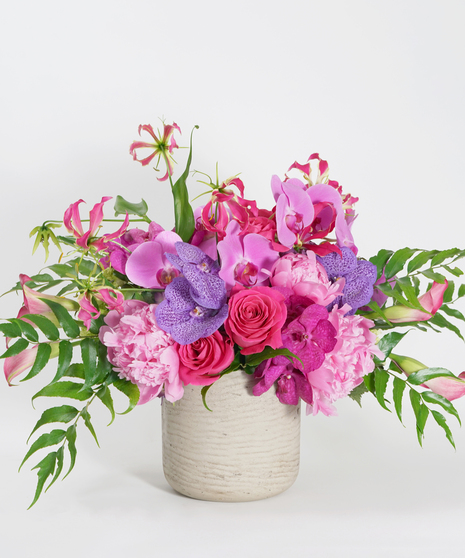 purple hydrangea, pink peonies, and fuchsia and hot pink orchids arranged in a grey stone container with textural accents