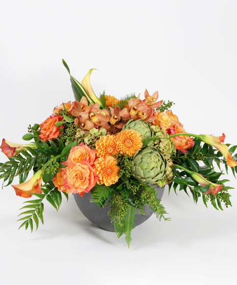 orange rose, dahlias and calla lilies accented with textural greens designed in a grey stone bowl