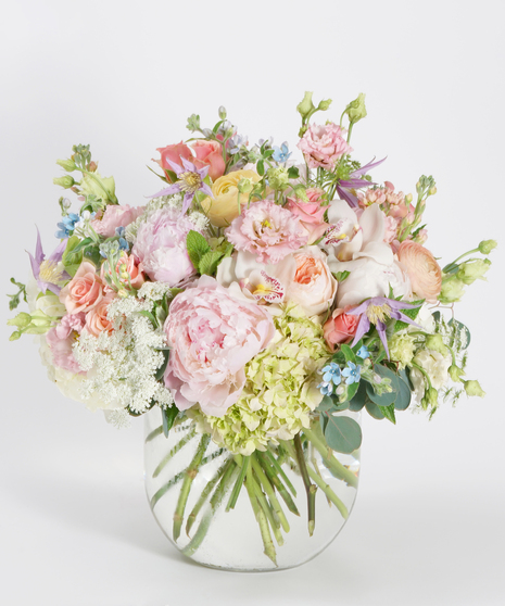 lush collection of peach roses, pink hydrangea, and light pink peonies arranged in a glass bowl