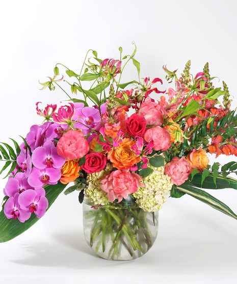 luxury floral design of pink orchids, coral peonies, orange snapdragon and gloriosa lilies arranged in a large glass bowl