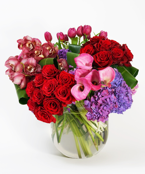 floral arrangement of red roses, purple hydrangea, pink calla lilies and burgundy orchids arranged in a large glass bowl