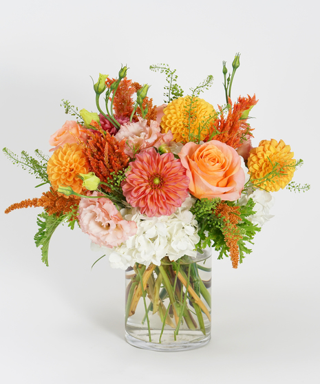 gardeny floral design of orange and peach dahlias, coral roses, and textural greens.