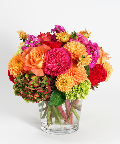 orange dahlias, hot pink garden roses and antique hydrangea arranged in a low glass vase