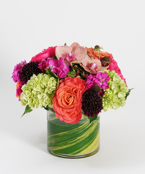 orange roses, hot pink stock and plum scabiosa arranged in a glass vase