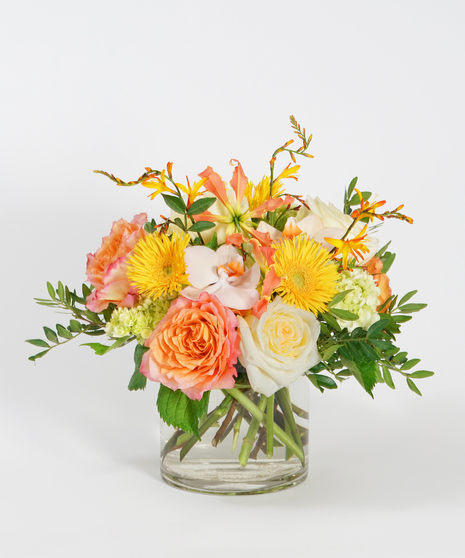 colorful floral design of tangerine roses, yellow spider gerbera daisies, and peach orchids accented with seasonal greens