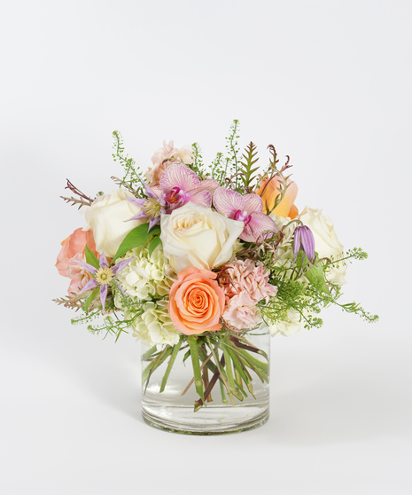 coral roses, white hydrangea and lavender clematis arranged in a clear glass vase