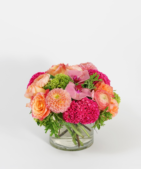 low and lush floral design of orange roses, peach dahlias, and coral orchids accented with seasonal greens