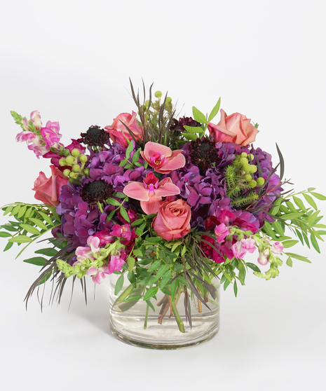 floral design of purple hydrangea, coral orchids, and lavender roses accented with delicate greens