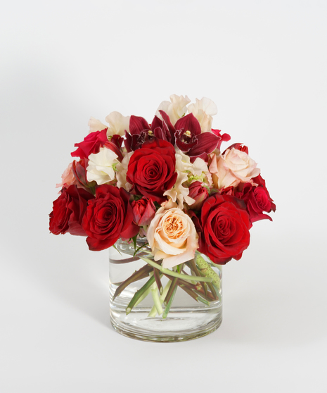 Valentine's Day arrangement featuring red roses, burgundy orchids and peach roses