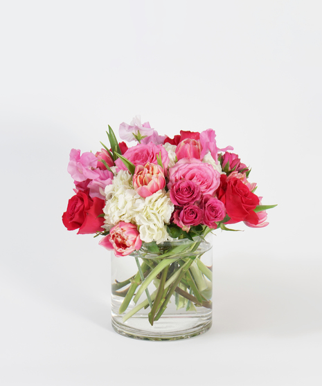 white hydrangea, pink roses and hot sweet pea arranged in a clear glass vase