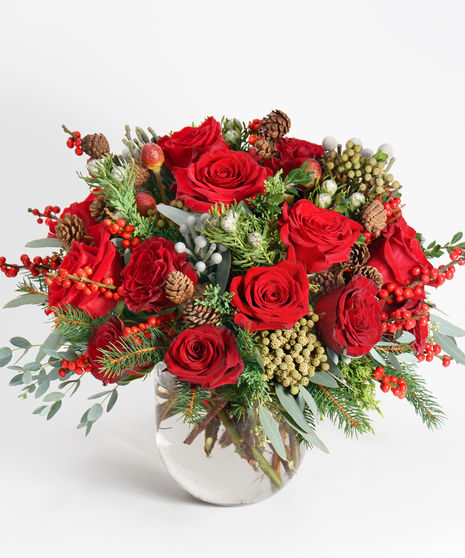 red roses and unique seasonal greens designed in a large glass bowl.
