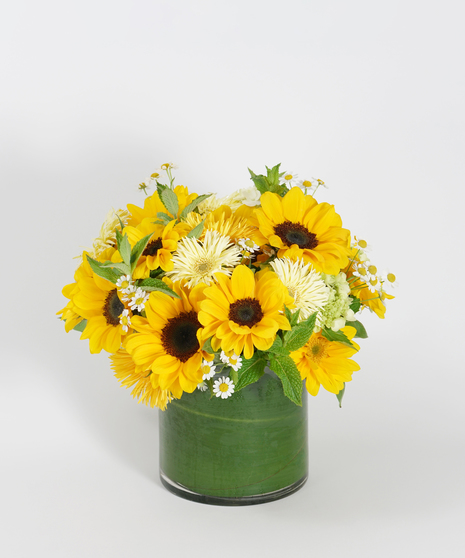 sunflowers and yellow spider gerbera daisies accented with chamomile and mint arranged in a glass vase