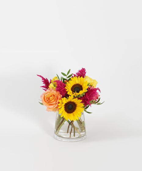 floral design of orange roses, sunflowers, and hot pink celosia
