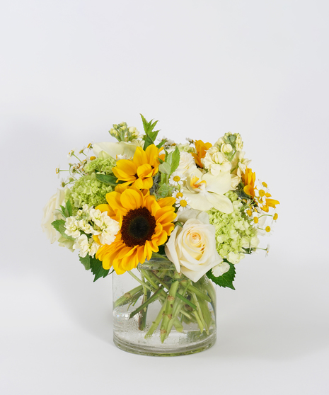 sunflowers, mini green hydrangea, and yellow orchids arranged in a clear glass vase