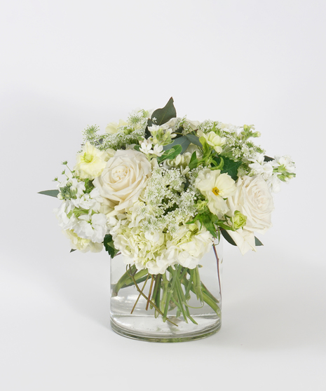 all white floral design with textural greens designed in a clear glass vase
