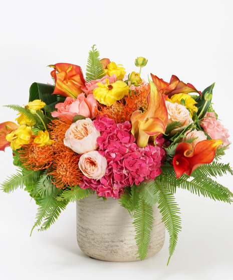 unique floral design of orange protea, mango calla lilies, and hot pink hydrangea arranged in a grey stone bowl