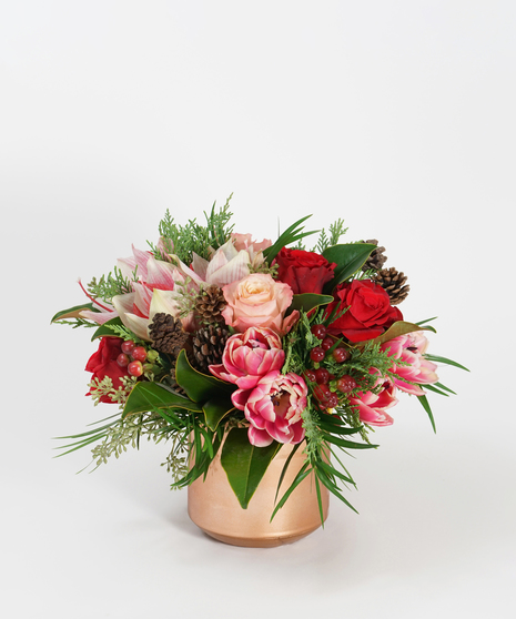 peppermint amaryllis, red roses, and pink tulips accented with hypericum berries and seasonal greens arranged in a copper vase