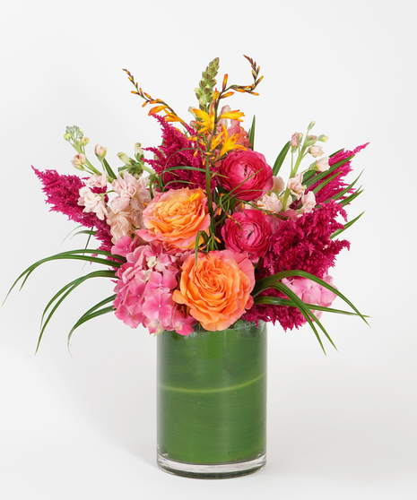 colorful floral design of hot pink ranunculus, orange roses, and pink hydrangea accented with orange snap dragon