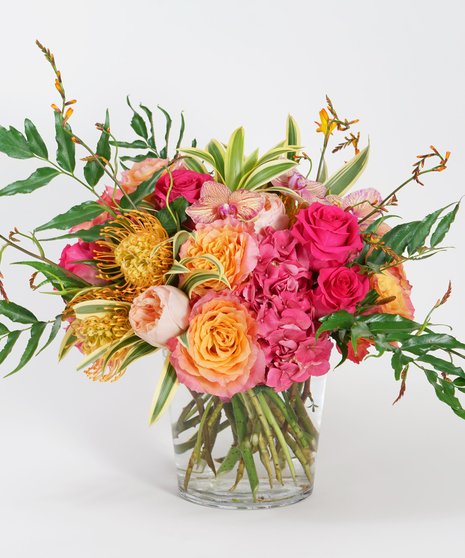 colorful floral design featuring pink hydrangea, orange protea, peach garden roses and orchids accented with textural summer greens