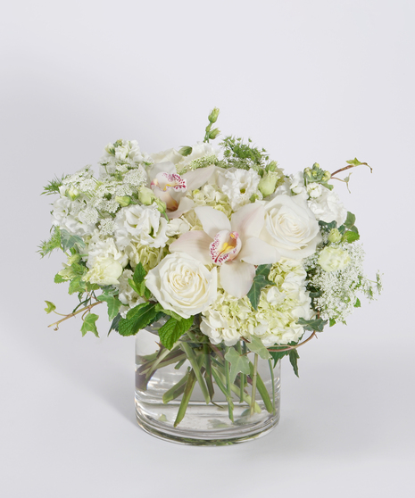 all white floral design with textural greens designed in a clear glass vase