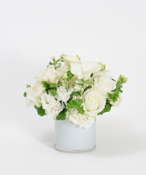 low and lush collection of white roses, white hydrangea, and orchids in a glass vase